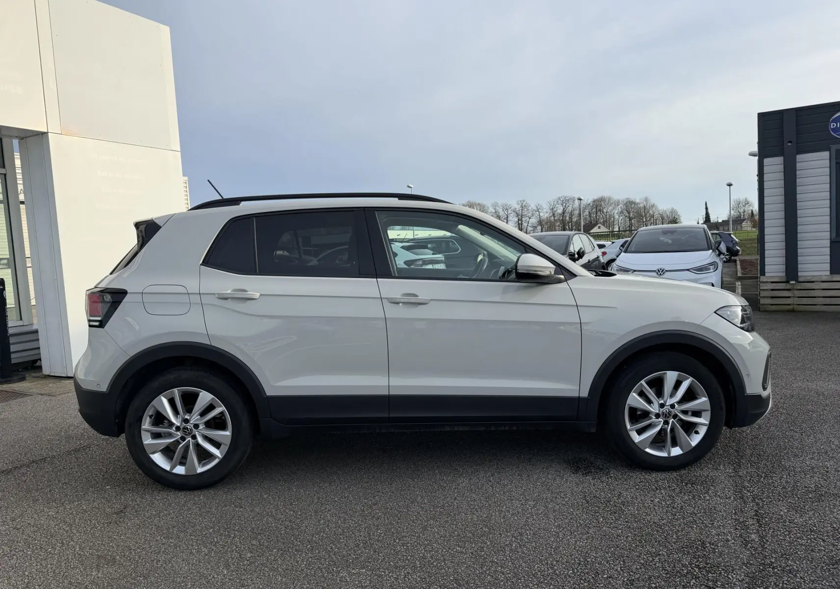 Vue latérale droite d'un Volkswagen T-Cross gris avec jantes alliage et vitres surteintées, stationné en extérieur.