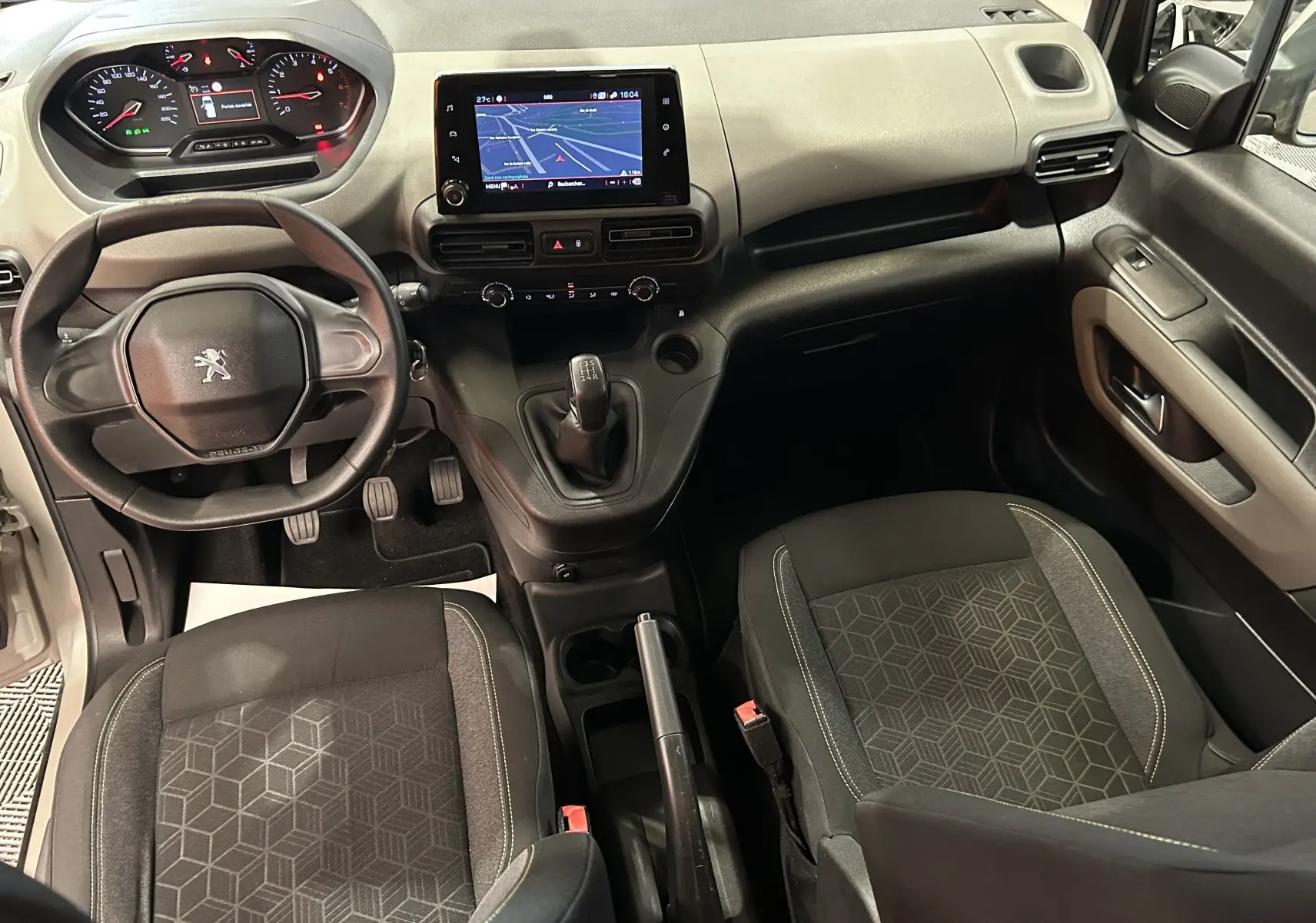 Vue intérieure avant du Peugeot Rifter 2019 gris sable, avec tableau de bord, volant, boîte manuelle et écran GPS tactile allumé.
