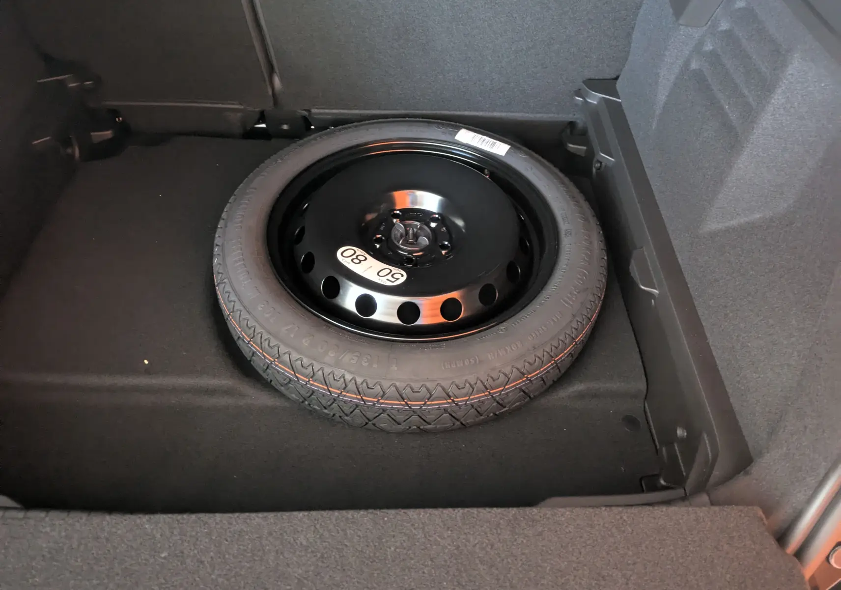 Roue de secours noire installée dans le coffre d'un Renault Symbioz hybride 2025, vue en plongée rapprochée.