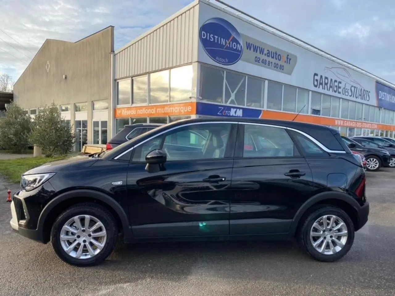 Opel Crossland noir métal vue de profil côté gauche, stationné devant un garage avec vitres teintées et jantes argentées.