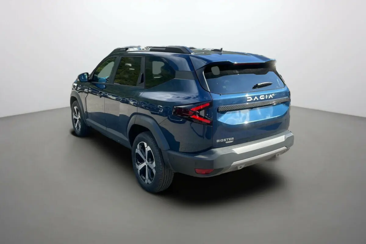 Vue 3/4 arrière droite d'un Dacia Bigster bleu indigo avec barres de toit et jantes alu 18 pouces.