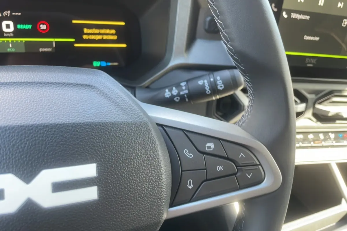 Gros plan sur le volant cuir de la DACIA BIGSTER Hybrid 155 Journey City avec commandes multifonctions et tableau de bord digital.