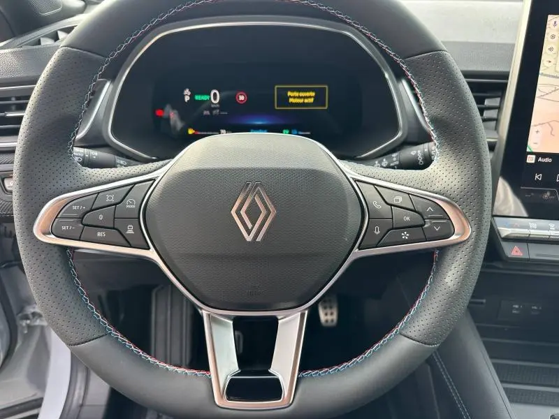 Volant en cuir perforé avec surpiqûres tricolores du Renault Captur 1.8 E-Tech hybride 2026, tableau de bord numérique en arrière-plan.