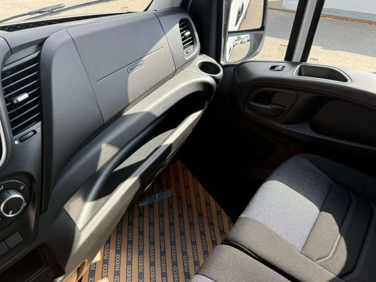 Intérieur côté passager de l’IVECO Daily blanc, vue sur tableau de bord et siège tissu gris foncé.