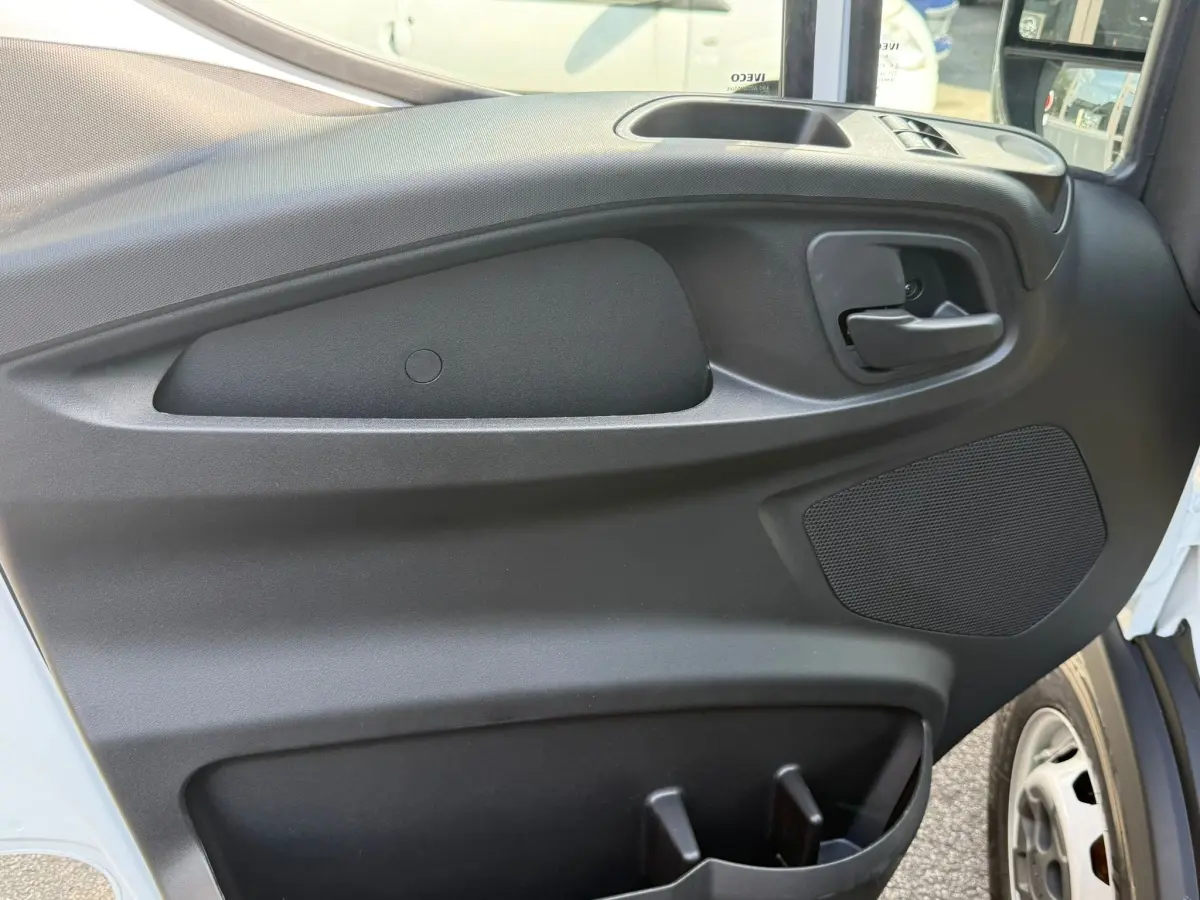 Vue rapprochée de la porte avant droite noire du fourgon Iveco Daily blanc, avec poignée et haut-parleur intégrés.