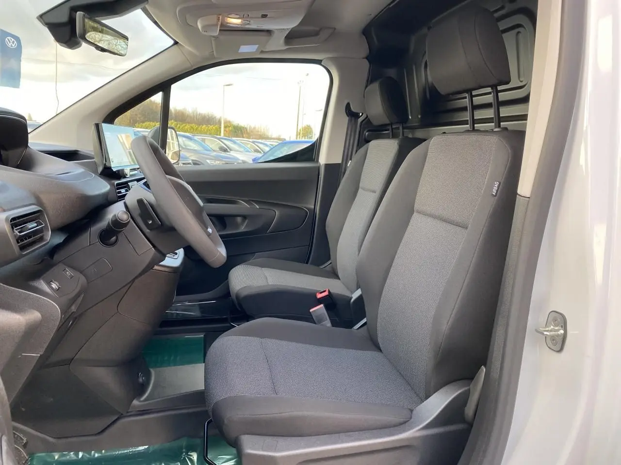 Vue intérieure côté conducteur du Peugeot Partner Fourgon blanc 2025, sièges tissu gris et tableau de bord moderne.