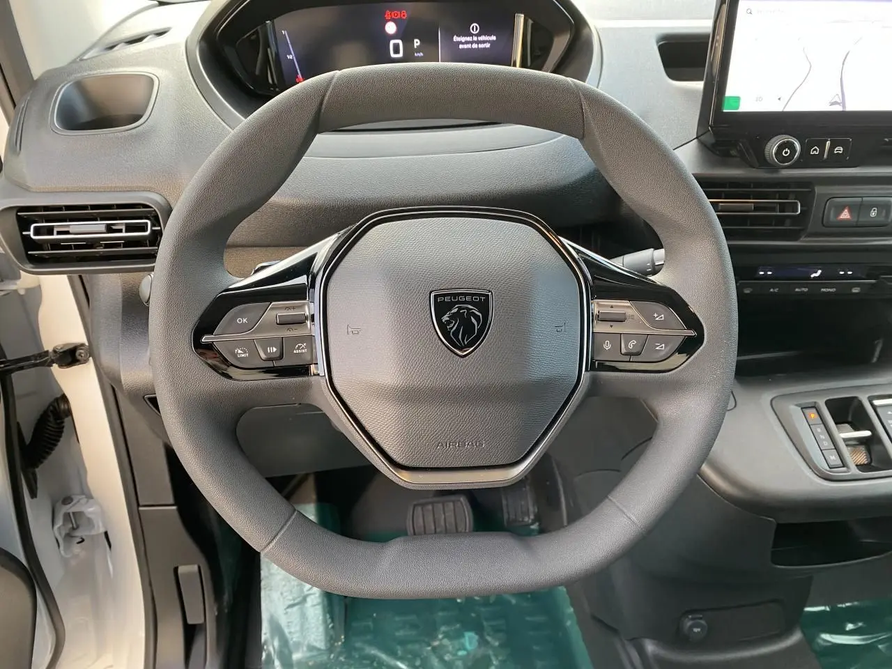 Vue intérieure centrée sur le volant Peugeot noir du Partner Fourgon blanc avec tableau de bord numérique et écran tactile.