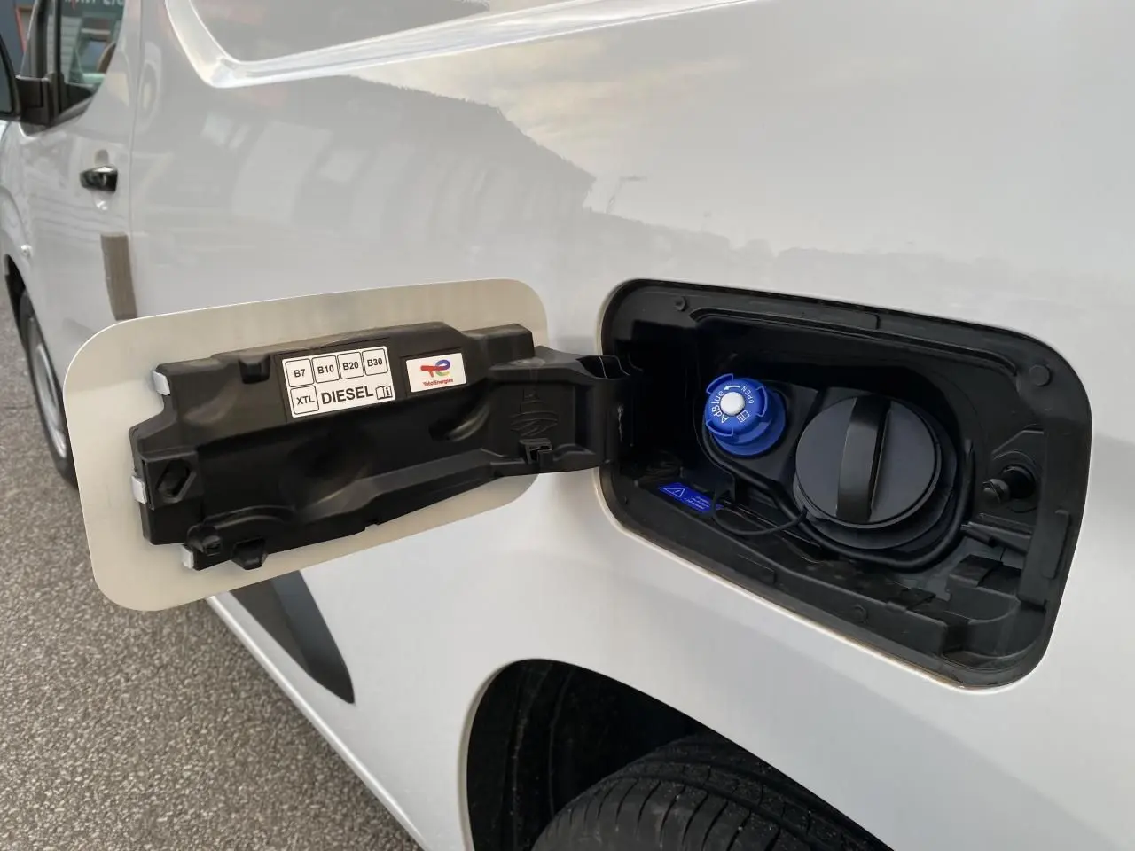 Vue rapprochée de la trappe à carburant côté gauche d'un Peugeot Partner Fourgon blanc avec bouchon diesel bleu.