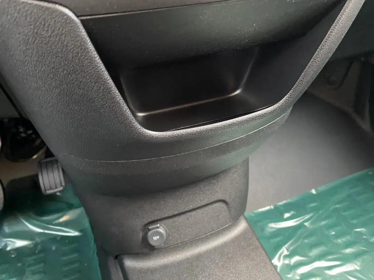 Gros plan sur la console centrale noire du Peugeot Partner Fourgon 2025 avec prise 12V et tapis de protection vert.