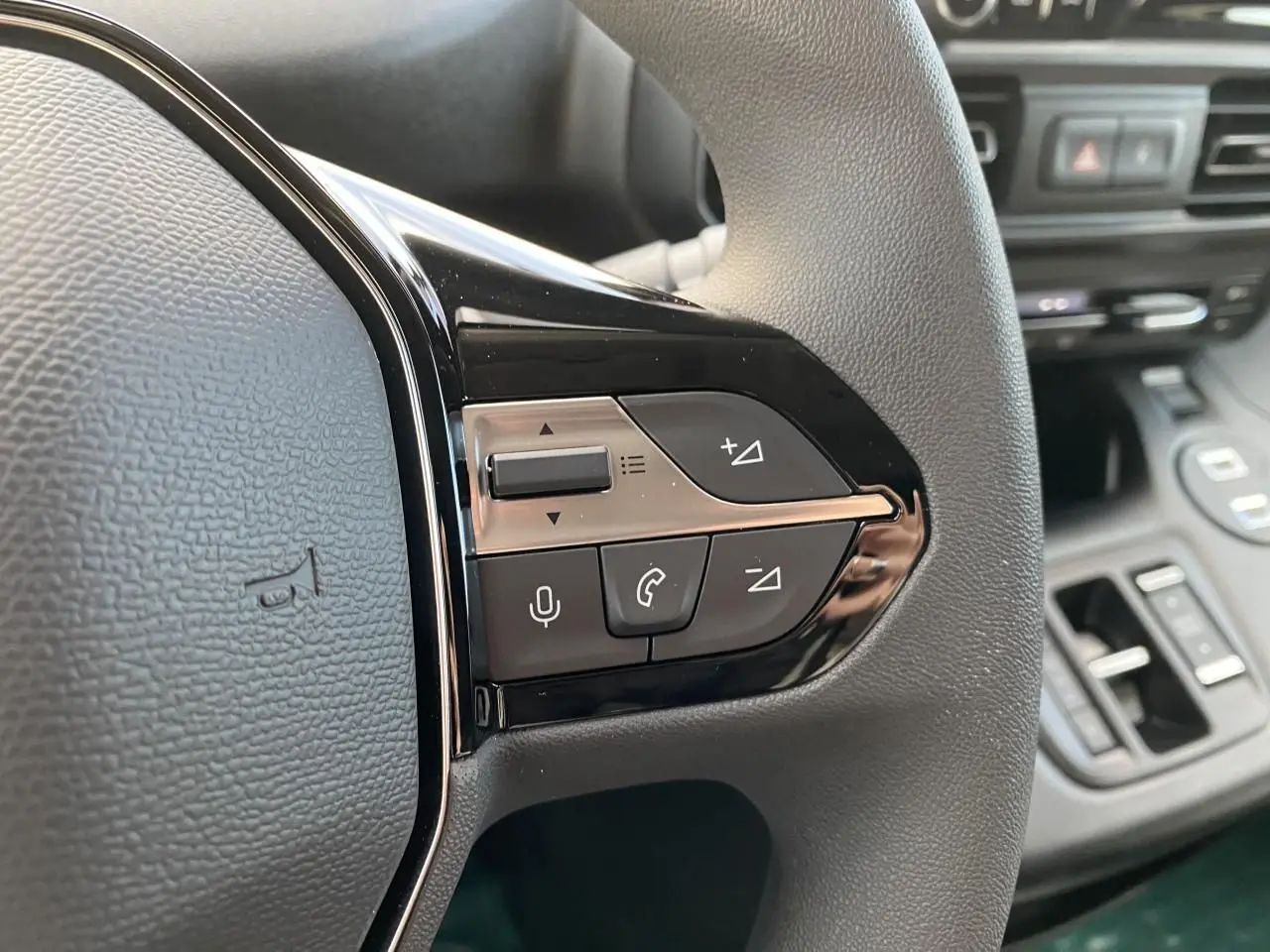 Gros plan sur les commandes multifonctions à droite du volant noir du Peugeot Partner Fourgon blanc, avec tableau de bord flou en arrière-plan.