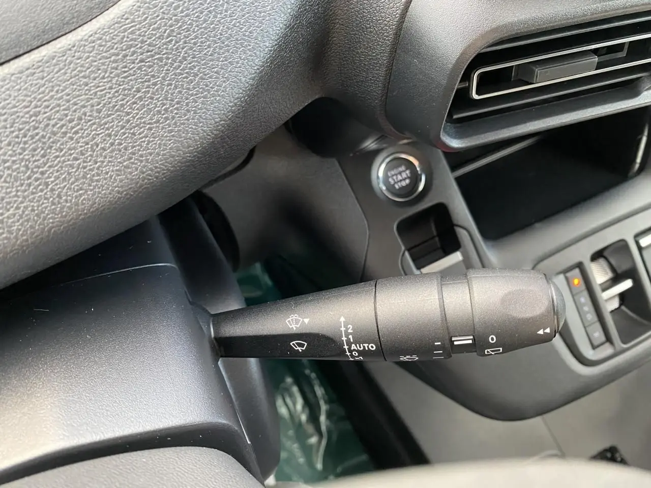 Gros plan sur la commande d’essuie-glace à gauche du volant dans l’habitacle noir du Peugeot Partner Fourgon blanc.