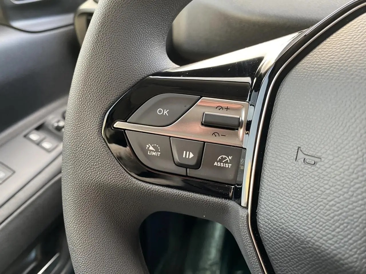 Gros plan sur les commandes de régulateur de vitesse au volant noir du Peugeot Partner Fourgon blanc, côté conducteur.