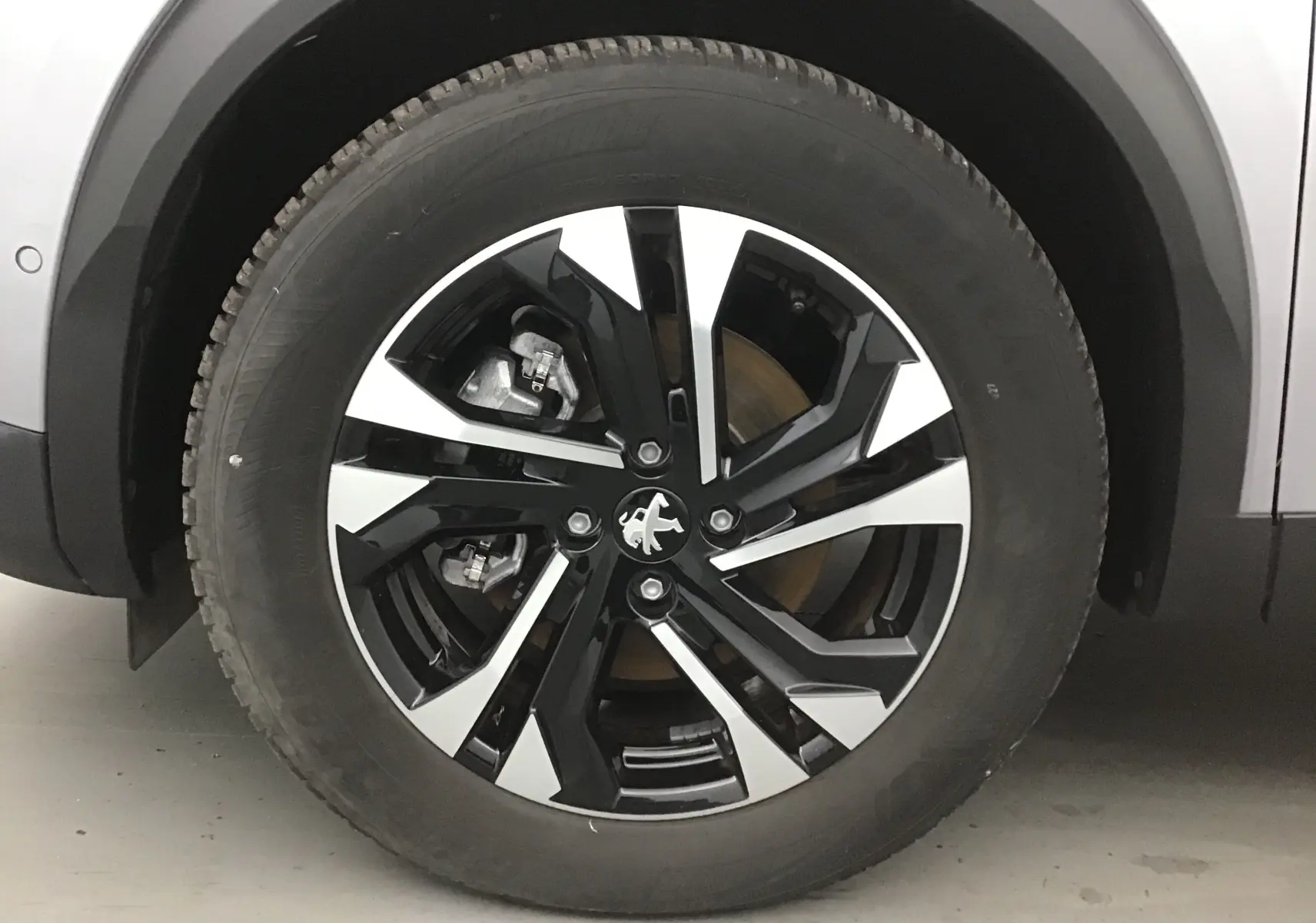 Gros plan sur la roue avant gauche du Peugeot 2008 électrique gris Artense, jante alliage noire et argentée au design moderne.