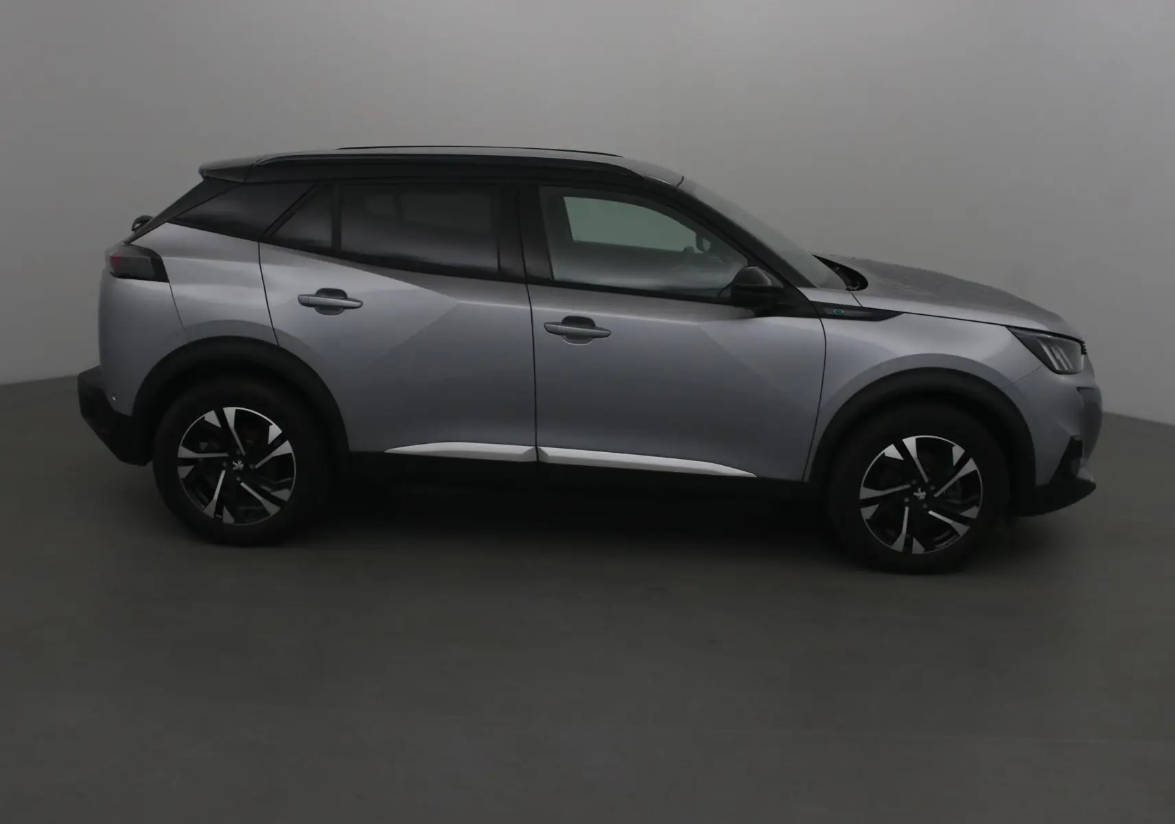 Profil côté gauche du Peugeot 2008 électrique 2022 en gris Artense avec toit noir et jantes noires.