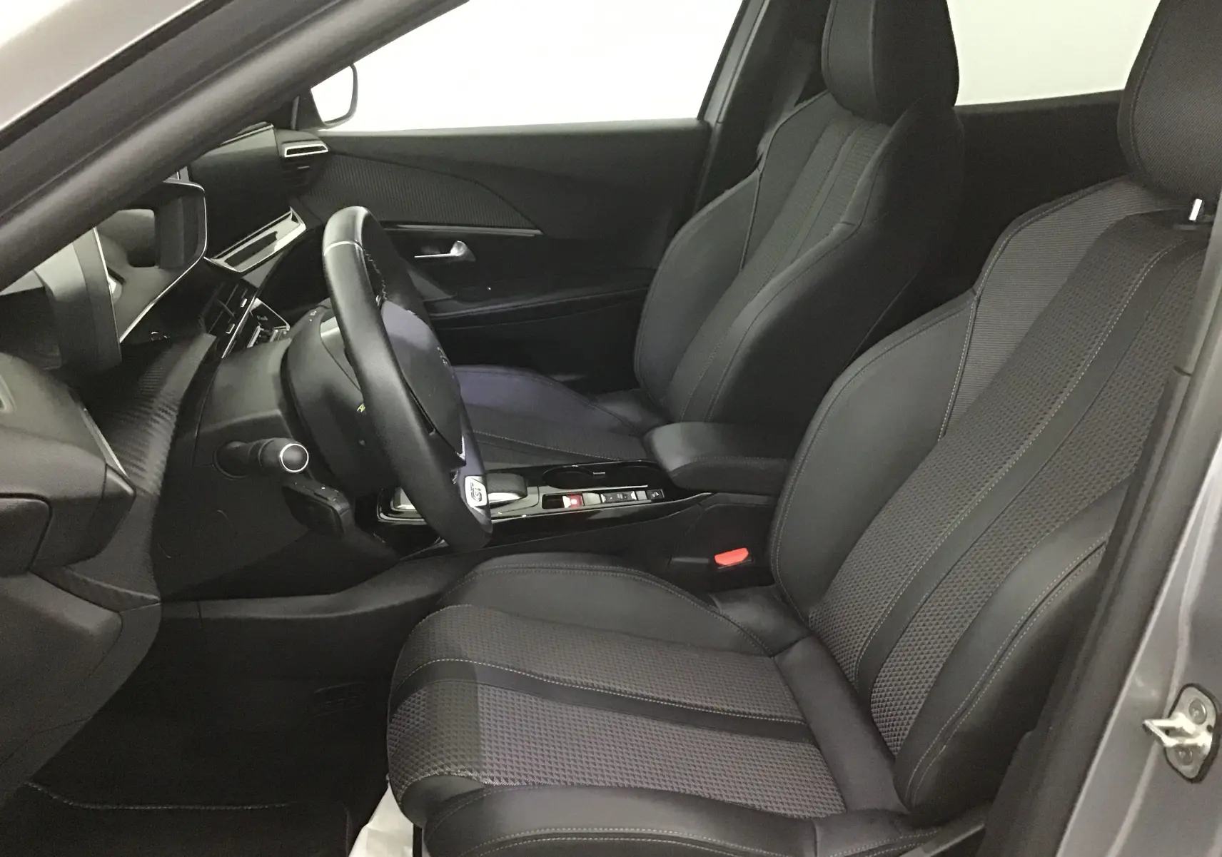 Intérieur côté gauche du Peugeot 2008 électrique gris, sièges en cuir noir et tableau de bord moderne avec volant multifonction.