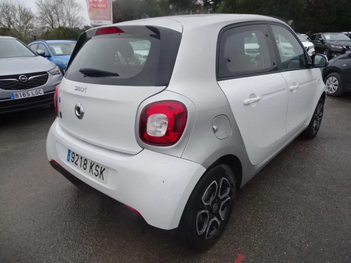 Vue 3/4 arrière droite d'une Smart Forfour électrique blanche avec jantes alliage bicolores et logo smart EQ visible.