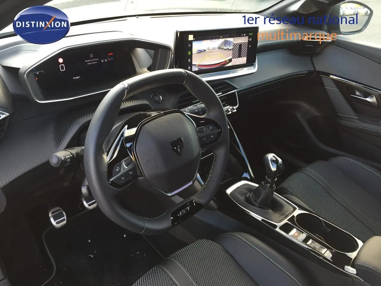 Intérieur de la Peugeot 208 2025, vue du poste de conduite avec volant GT, écran tactile et levier de vitesse manuel.