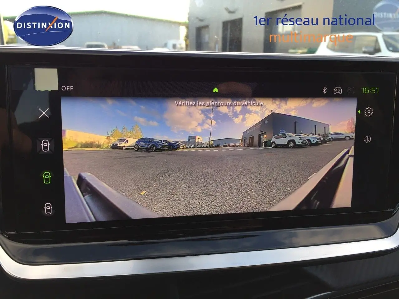 Vue de la caméra de recul du Peugeot 208 gris Artense, affichant le parking et plusieurs véhicules en arrière-plan.