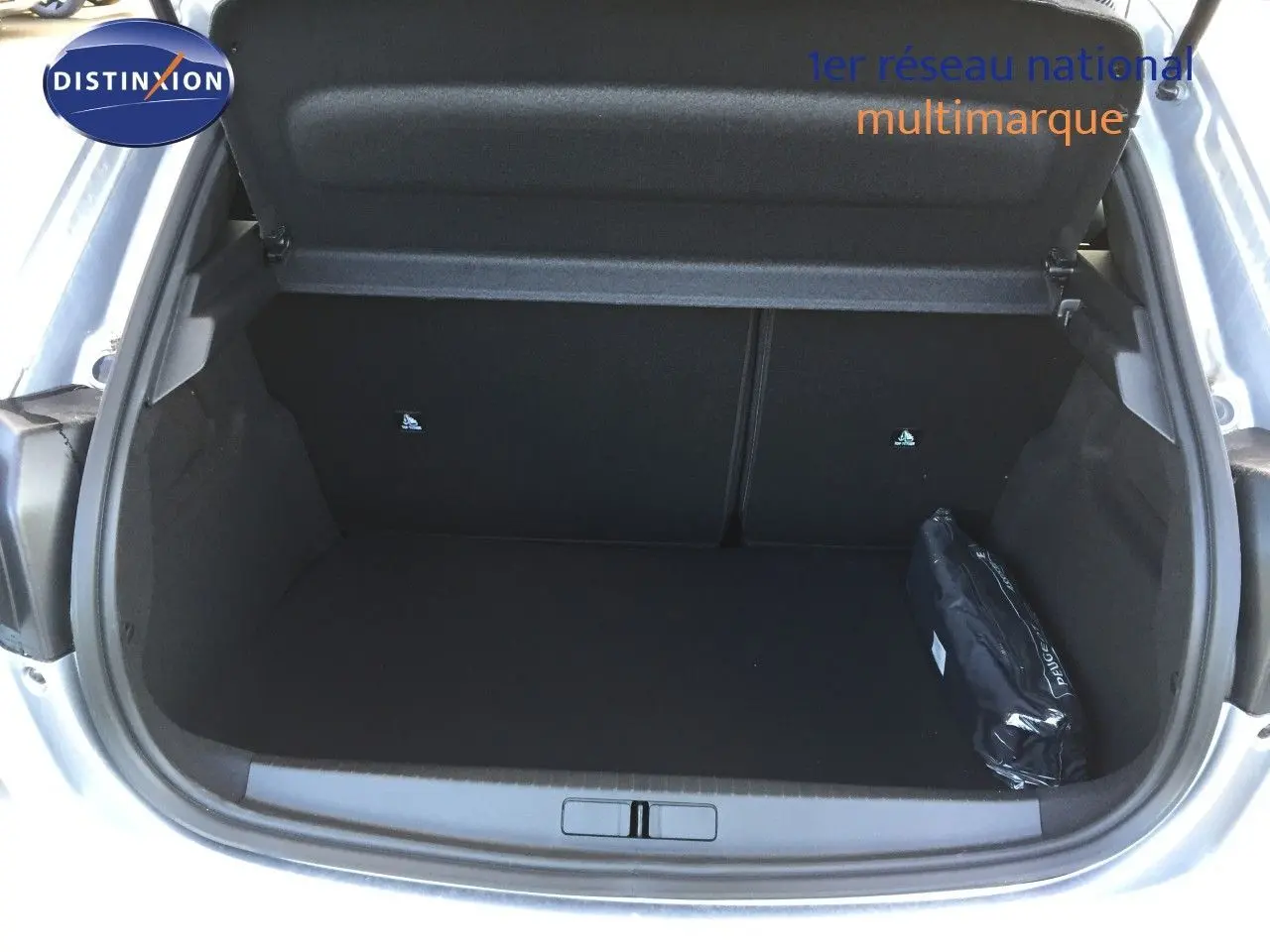 Coffre ouvert d'une Peugeot 208 gris Artense métal, montrant un espace de chargement vide avec une trousse noire sur le côté droit.