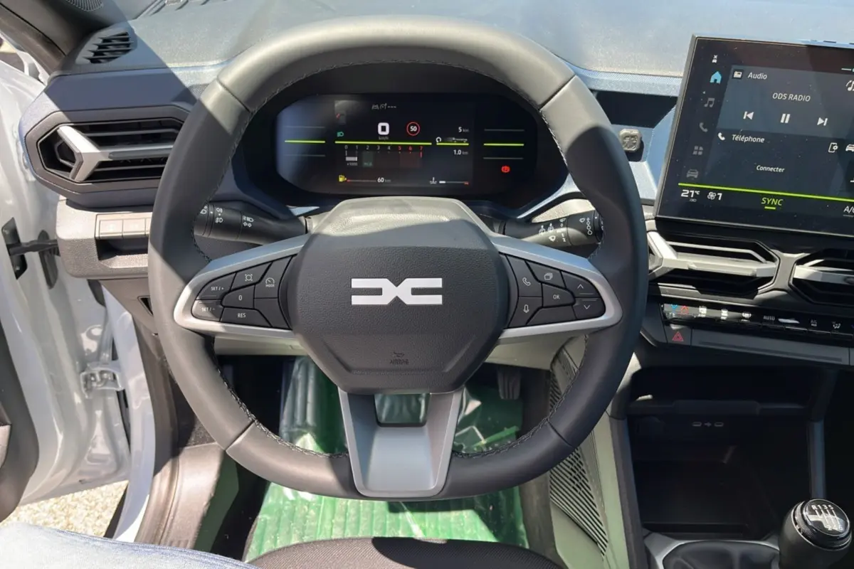 Vue rapprochée du volant cuir et du tableau de bord numérique du Dacia Bigster blanc glacier 2025, version mild hybrid.