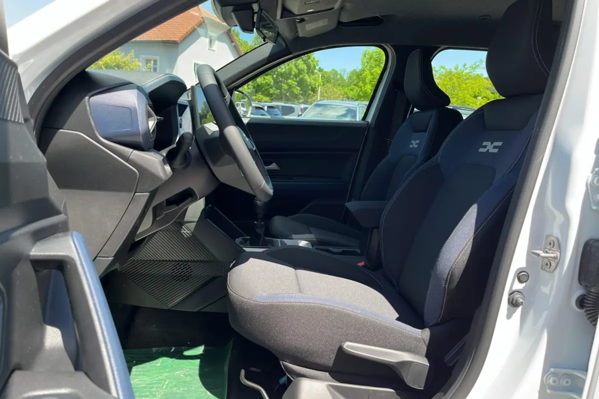 Intérieur du DACIA BIGSTER blanc glacier, vue côté gauche sur les sièges avant avec logo brodé et volant multifonction.