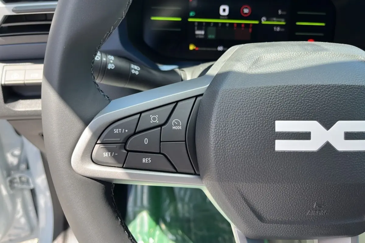 Gros plan sur le volant cuir du Dacia Bigster 2025 blanc glacier, avec commandes multifonctions et tableau de bord numérique.