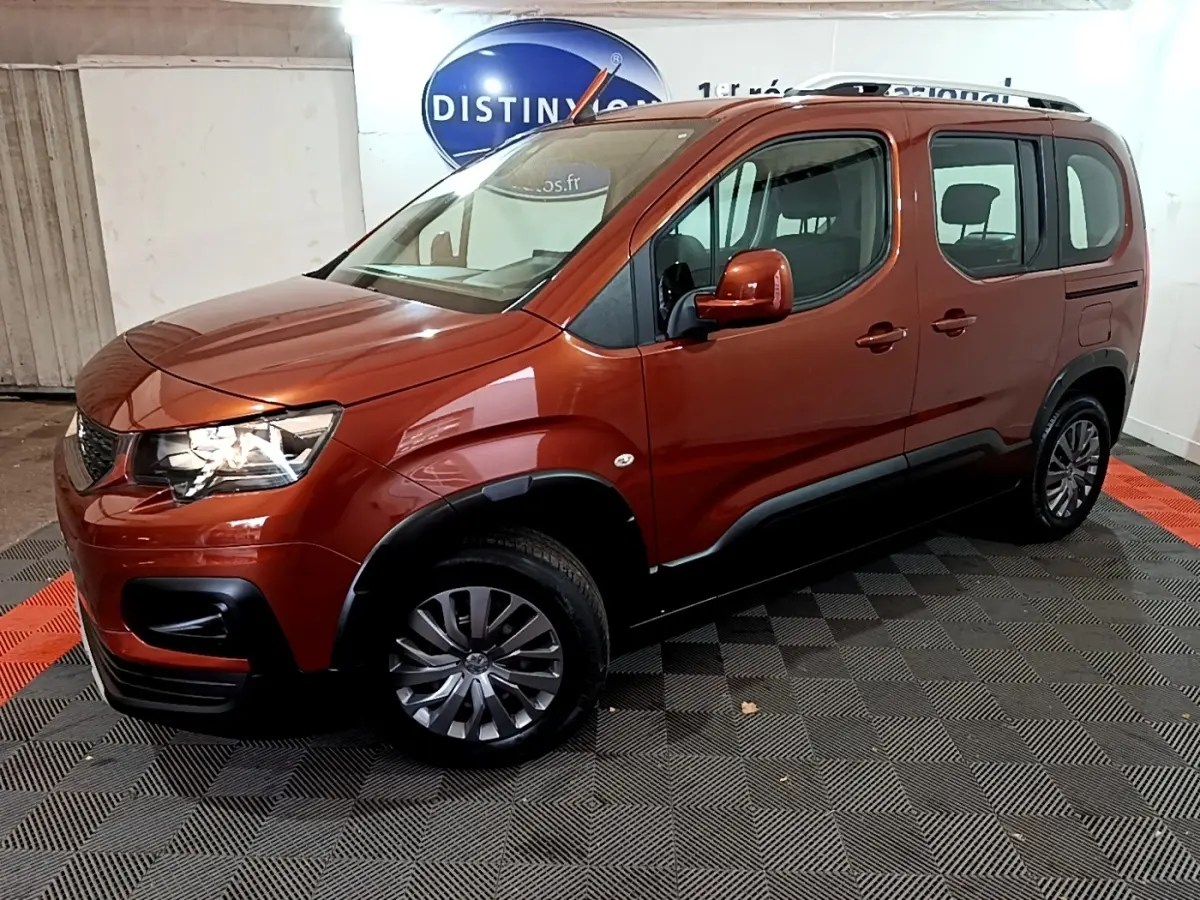 Peugeot Rifter BlueHDi 100 marron en 3/4 avant droit, avec barres de toit chromées et protections noires sur les bas de caisse.