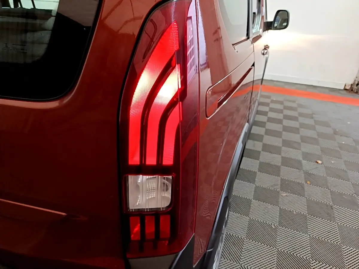 Gros plan sur le feu arrière droit rouge du Peugeot Rifter marron, avec reflet sur la carrosserie dans un parking intérieur.