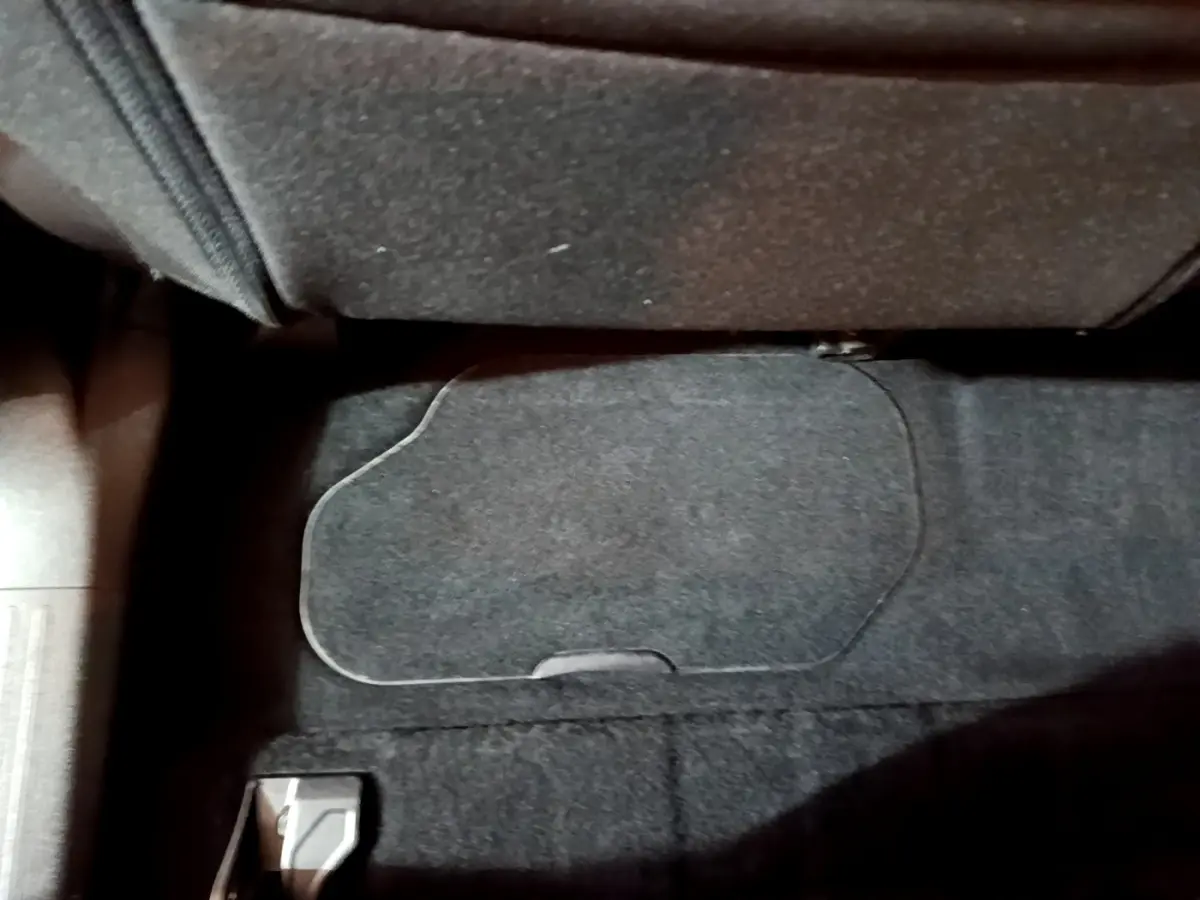 Gros plan sur le rangement sous le siège passager du Peugeot Rifter marron, moquette noire visible.