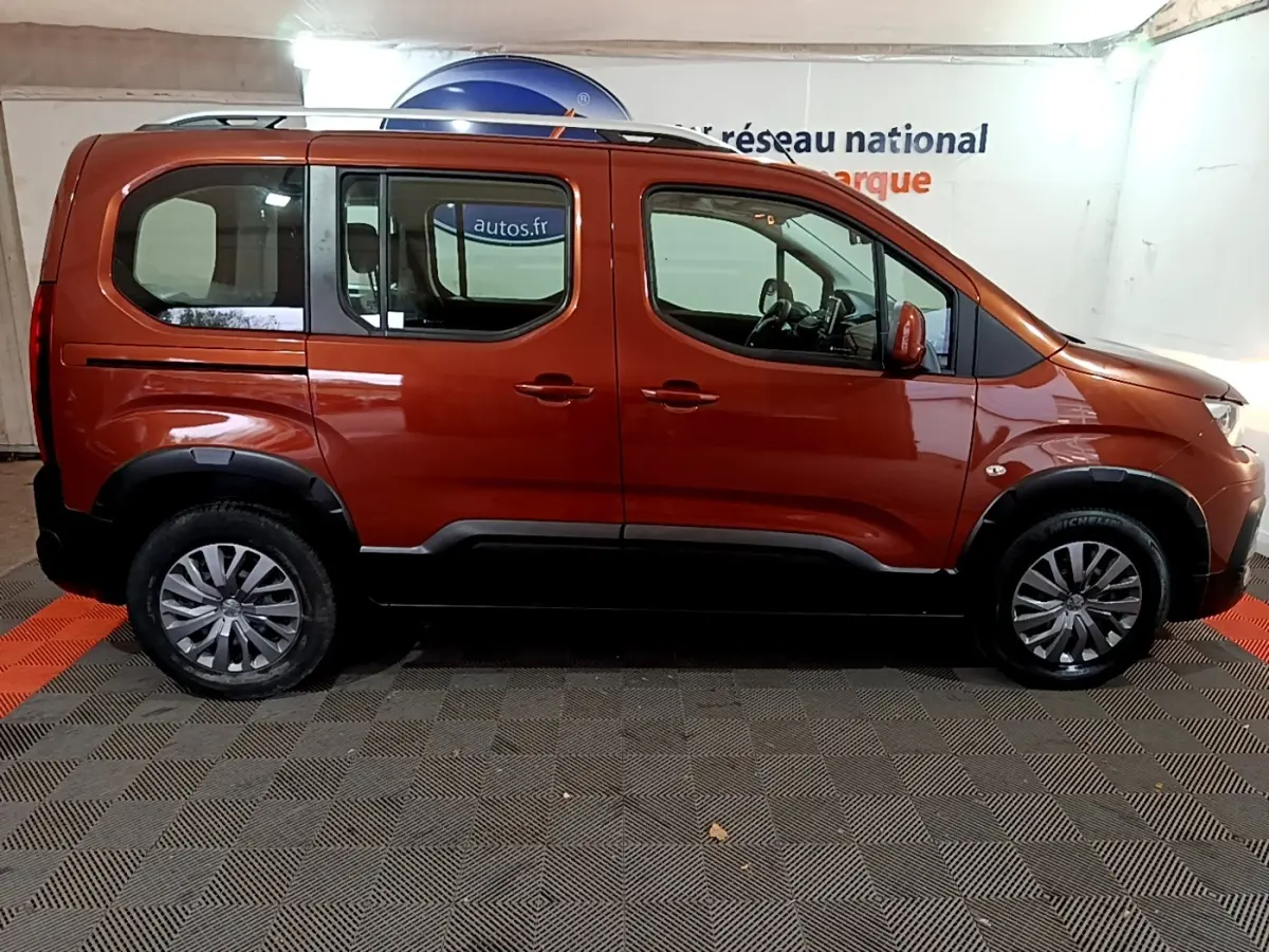 Profil droit d'un Peugeot Rifter marron 2019 avec barres de toit chromées et protections noires sur les passages de roues.