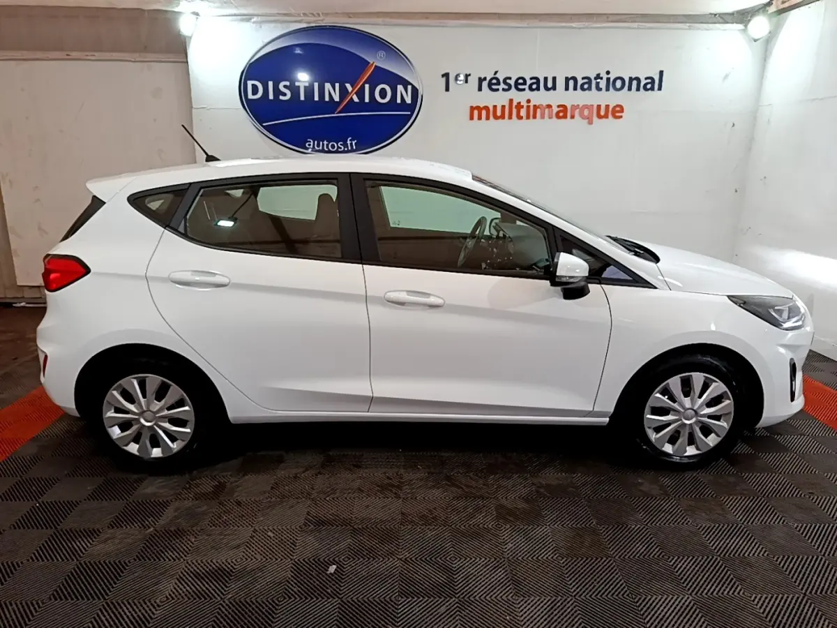 Vue de profil côté gauche d'une Ford Fiesta blanche 2022 dans un showroom avec logo Distinxion en arrière-plan.
