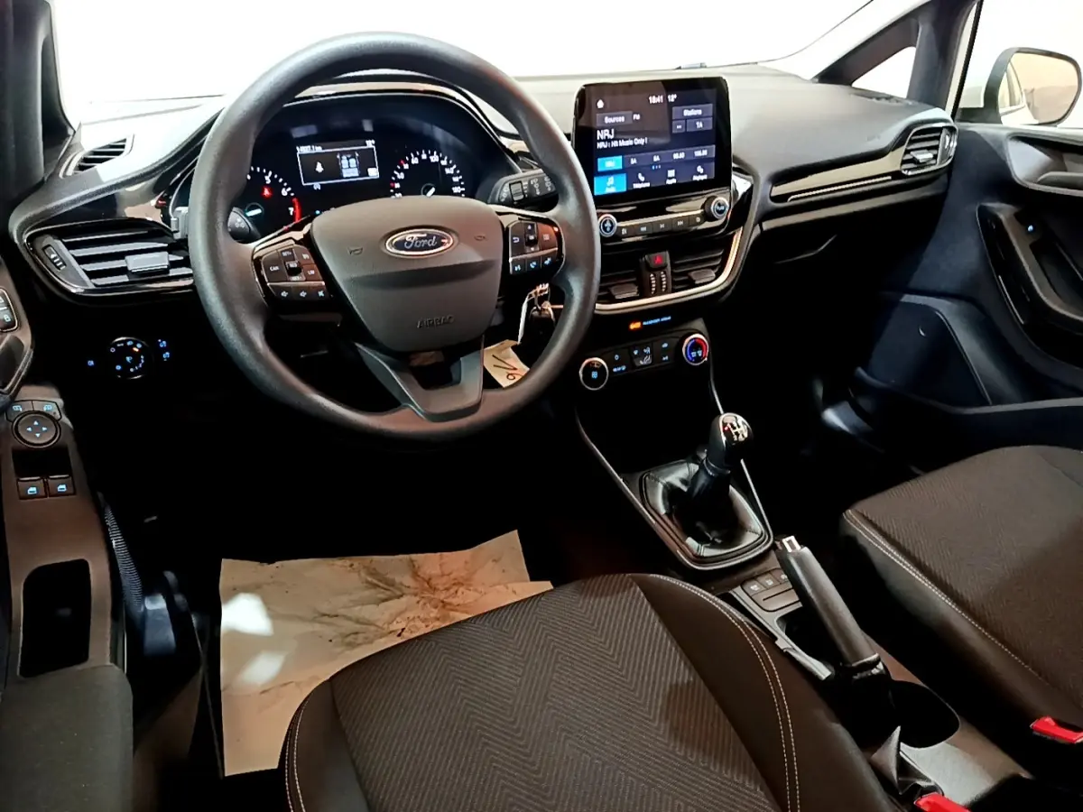 Vue intérieure avant de la Ford Fiesta blanche 2022, tableau de bord avec écran tactile et volant multifonctions.