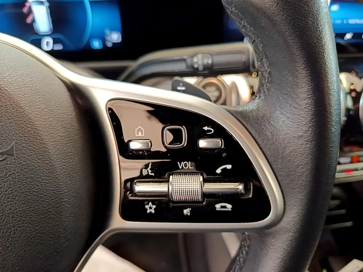 Gros plan sur la commande de volume et boutons multifonctions sur le côté gauche du volant cuir noir du Mercedes GLB 200 d gris foncé.