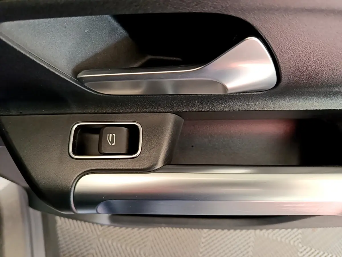 Détail de la poignée intérieure et bouton de lève-vitre sur la porte côté conducteur d’un Mercedes GLB gris foncé.