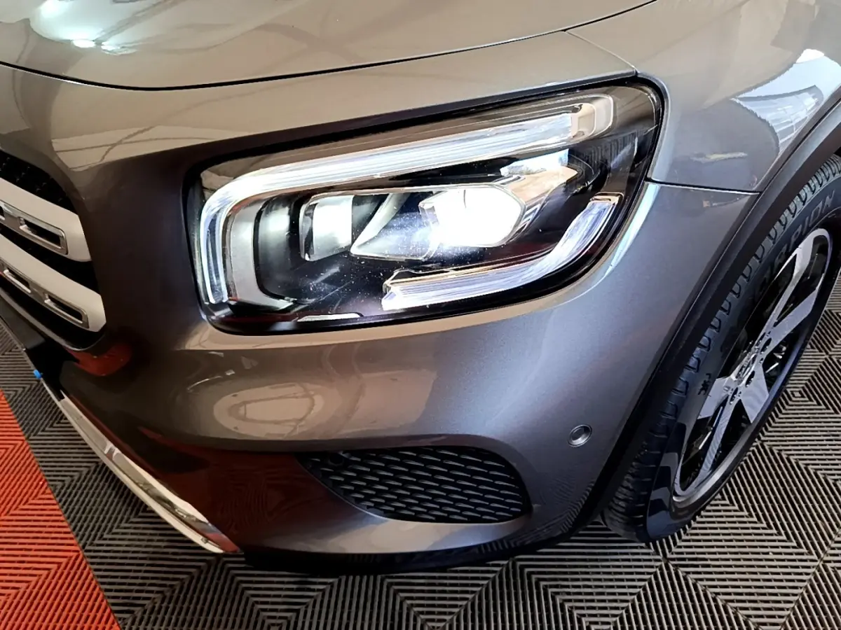 Gros plan sur le phare avant droit et la calandre d’un Mercedes GLB 200 d Business Line gris foncé.