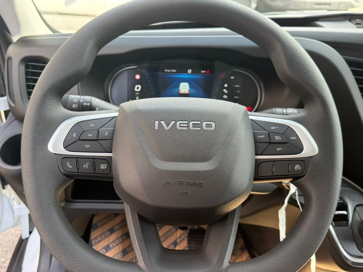 Vue rapprochée du volant noir de l’Iveco Daily 2026 avec commandes intégrées et tableau de bord numérique en arrière-plan.