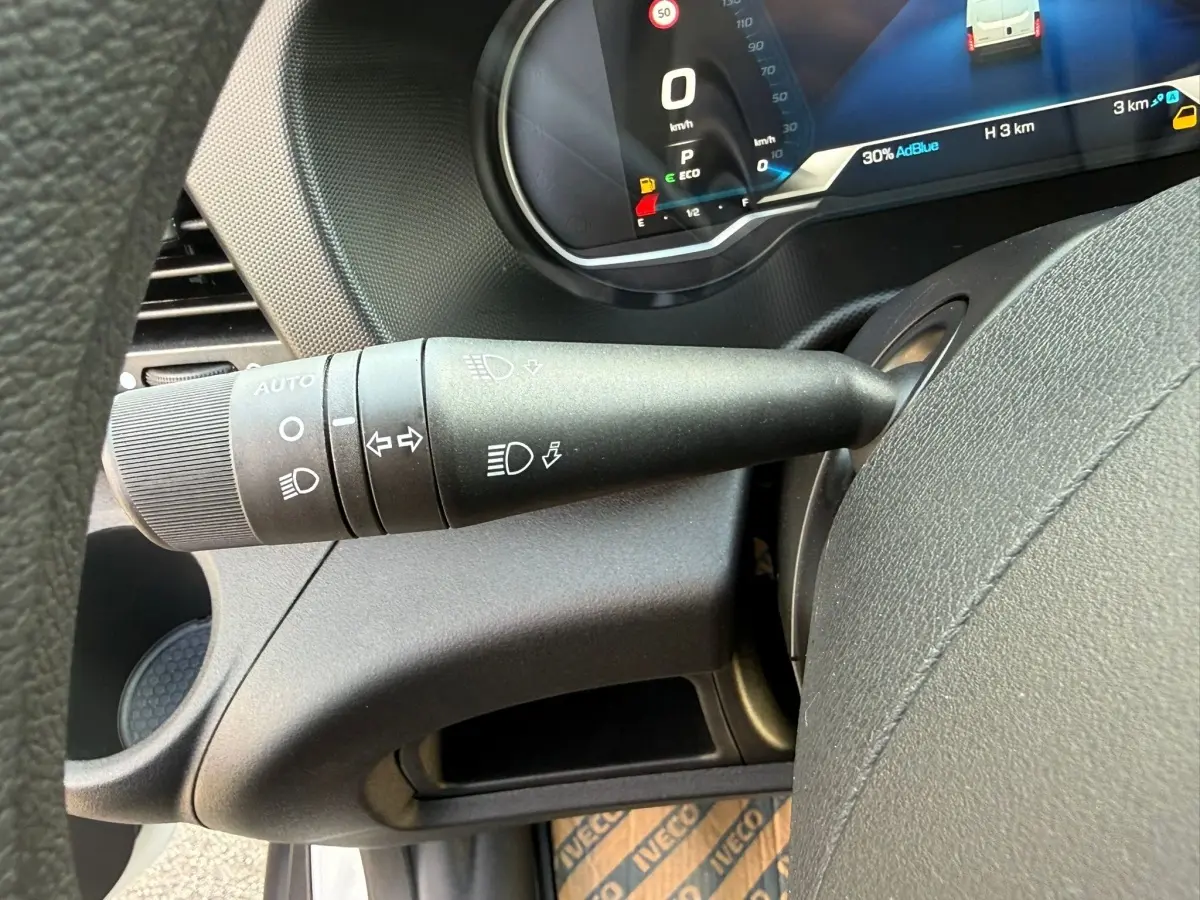 Gros plan sur la manette de commandes d’éclairage à gauche du volant dans l’habitacle du fourgon Iveco Daily blanc 2026.