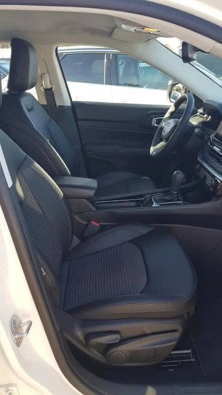 Vue intérieure côté conducteur du Jeep Compass blanc 2024, sièges noirs avec accoudoir central et tableau de bord moderne.