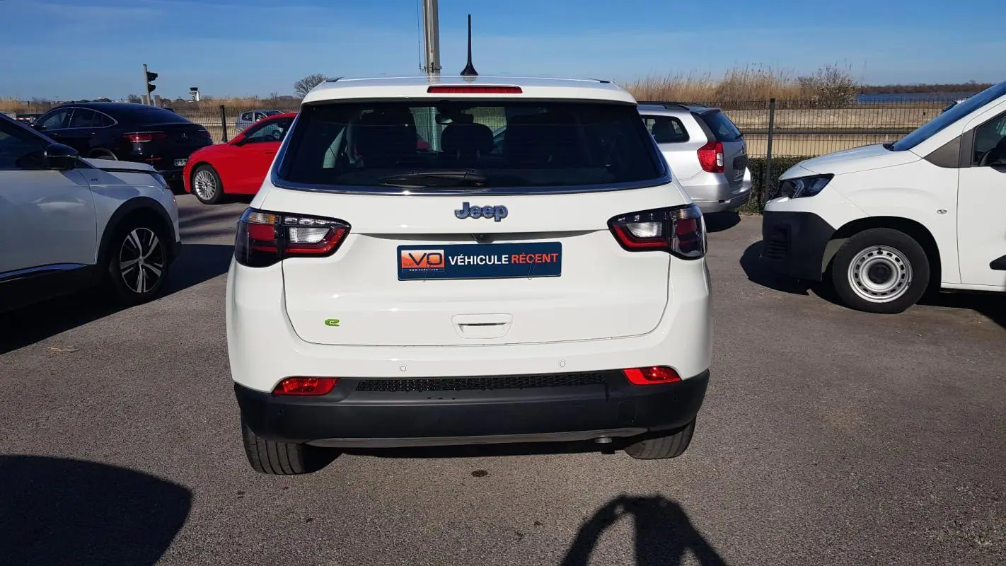 Vue arrière d'un Jeep Compass blanc 2024 avec feux LED et badge e-Hybrid sur un parking extérieur.