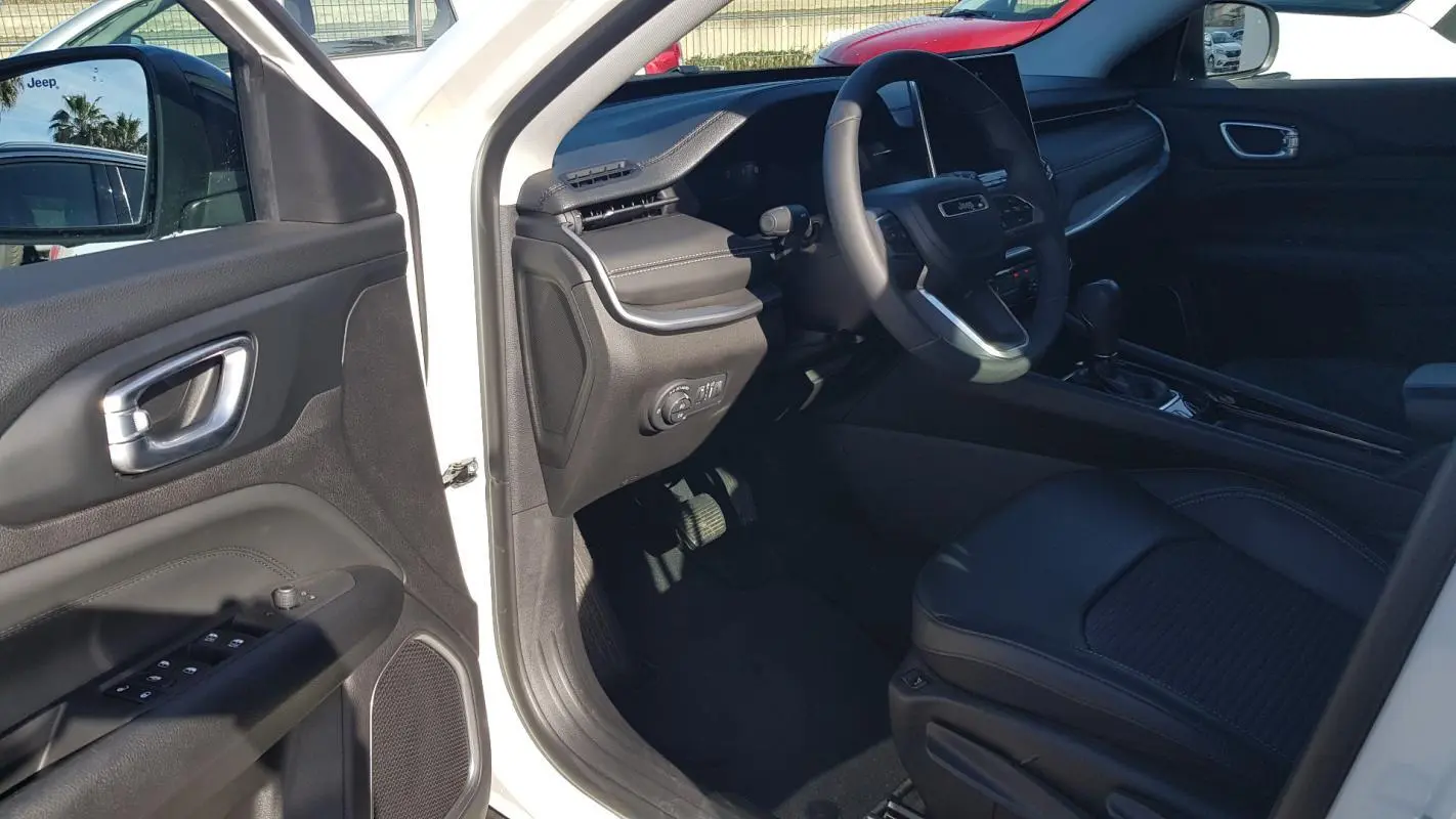 Intérieur du Jeep Compass blanc 2024 vu côté conducteur, avec tableau de bord et siège en cuir noir.