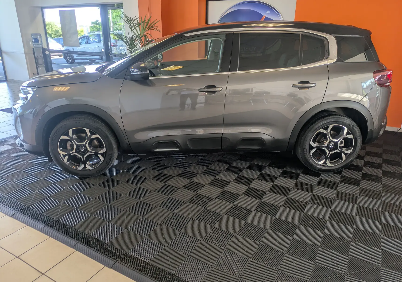 Profil latéral gauche d'un Citroën C5 Aircross hybride 2024 gris platinium avec toit noir, exposé en intérieur sur sol damier.