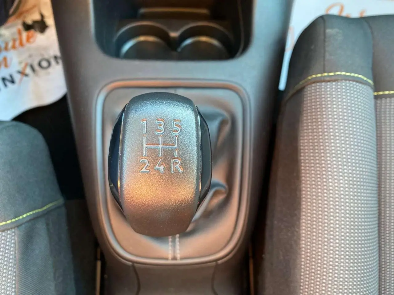 Le levier de vitesses manuel noir de la Citroën C3 2022, vue de dessus avec coutures blanches et siège gris à surpiqûres jaunes.