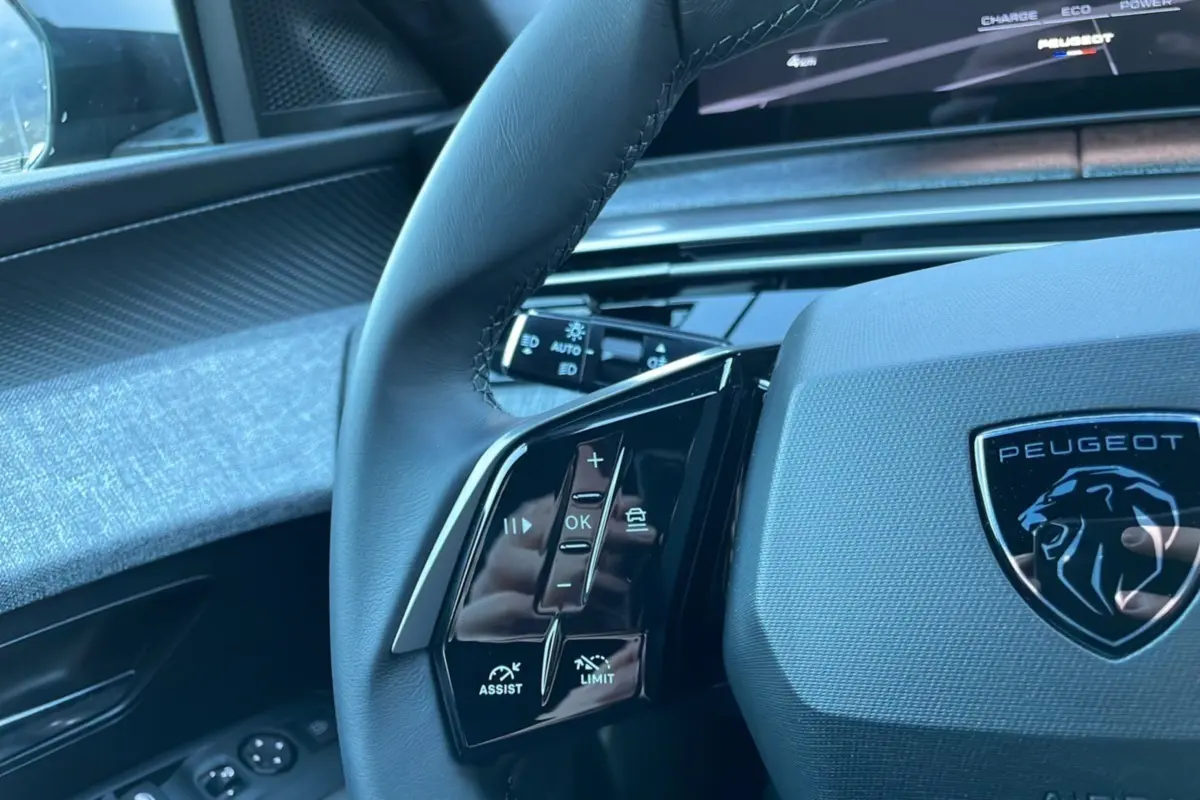 Gros plan sur le volant cuir du Peugeot 5008 gris titane 2025, avec commandes intégrées et logo lion central.