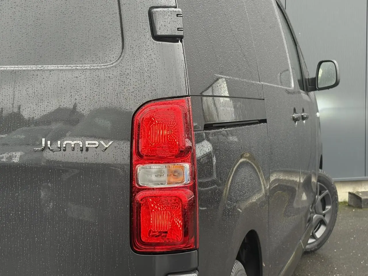 Vue arrière côté droit du Citroën Jumpy gris titane avec feux arrière rouges et portes tôlées sous la pluie.