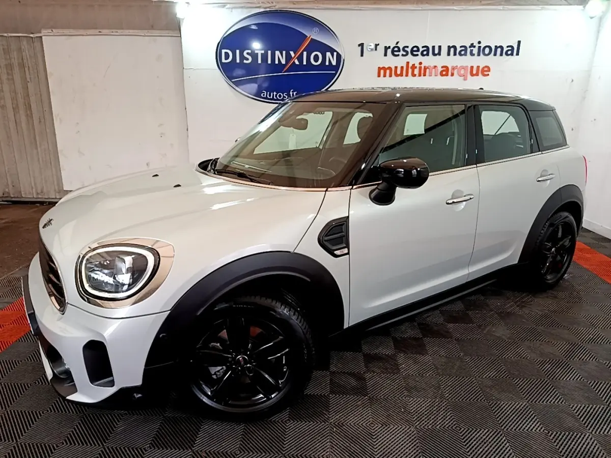 Vue 3/4 avant droit d'une MINI Countryman gris clair avec toit noir et jantes noires dans un showroom.