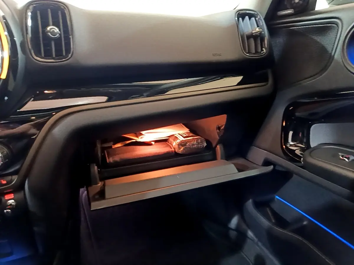 Intérieur du MINI Countryman 2022, vue côté passager sur la boîte à gants ouverte avec éclairage d’ambiance bleu.