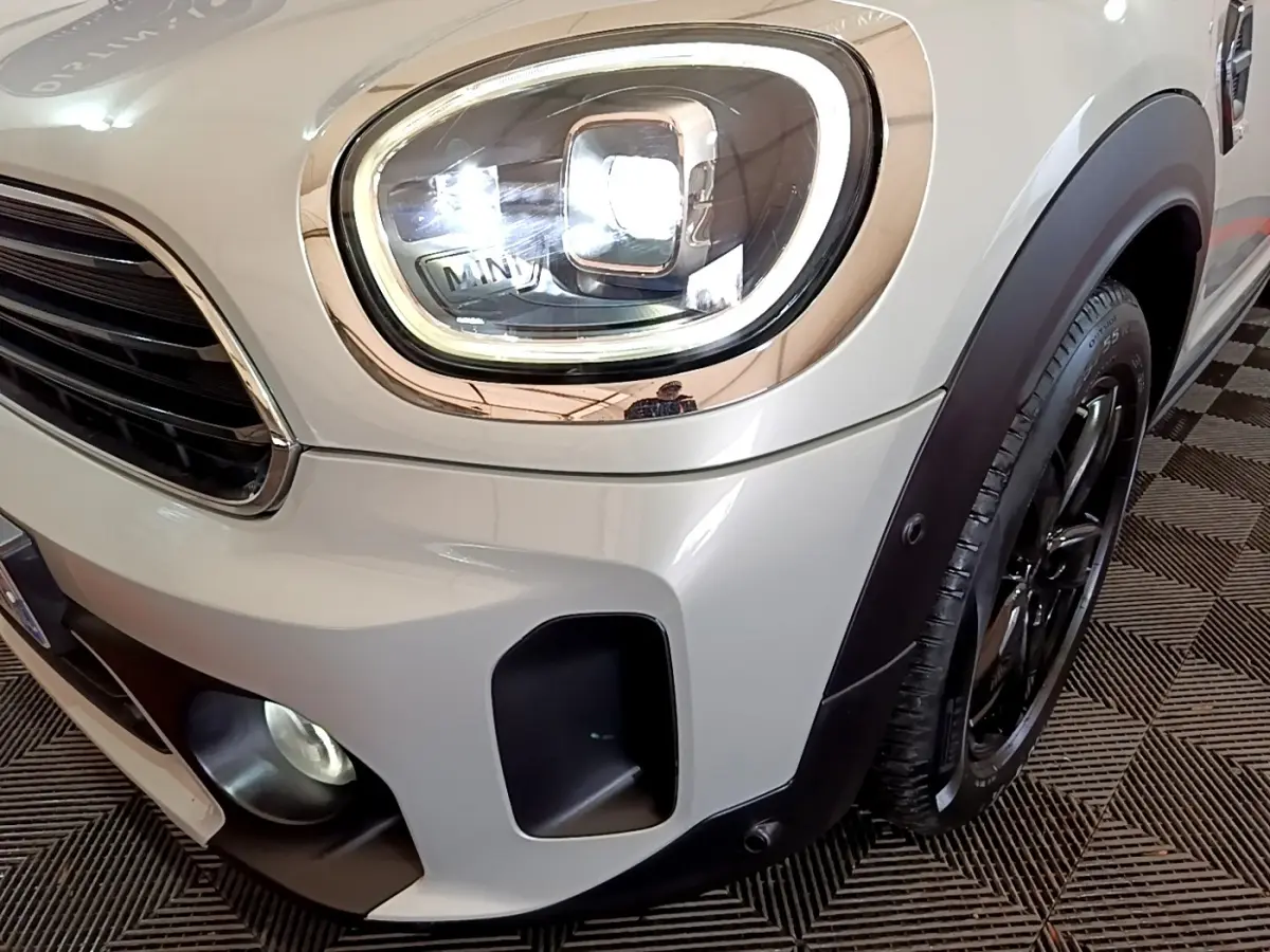 Gros plan sur le phare avant gauche et la roue d’une MINI Countryman gris clair avec détails noirs et éclairage LED.
