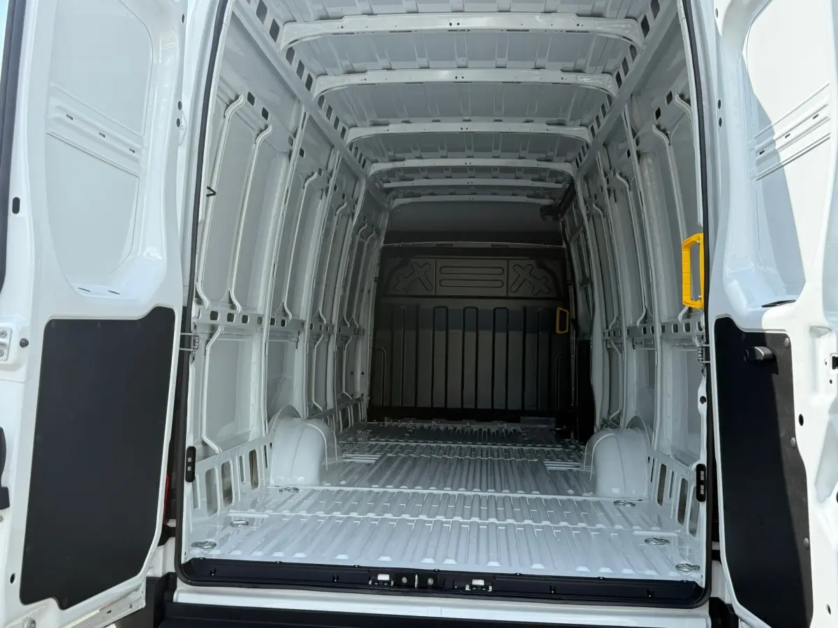 Vue intérieure arrière du fourgon Iveco Daily blanc 2026, montrant l'espace de chargement vide avec poignées jaunes aux portes ouvertes.