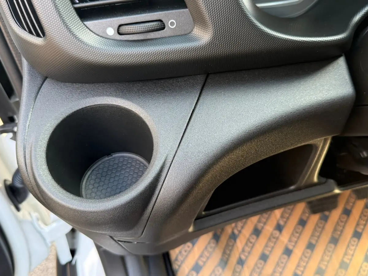 Détail intérieur montrant le porte-gobelet et le rangement côté gauche du tableau de bord d’un Iveco Daily blanc.