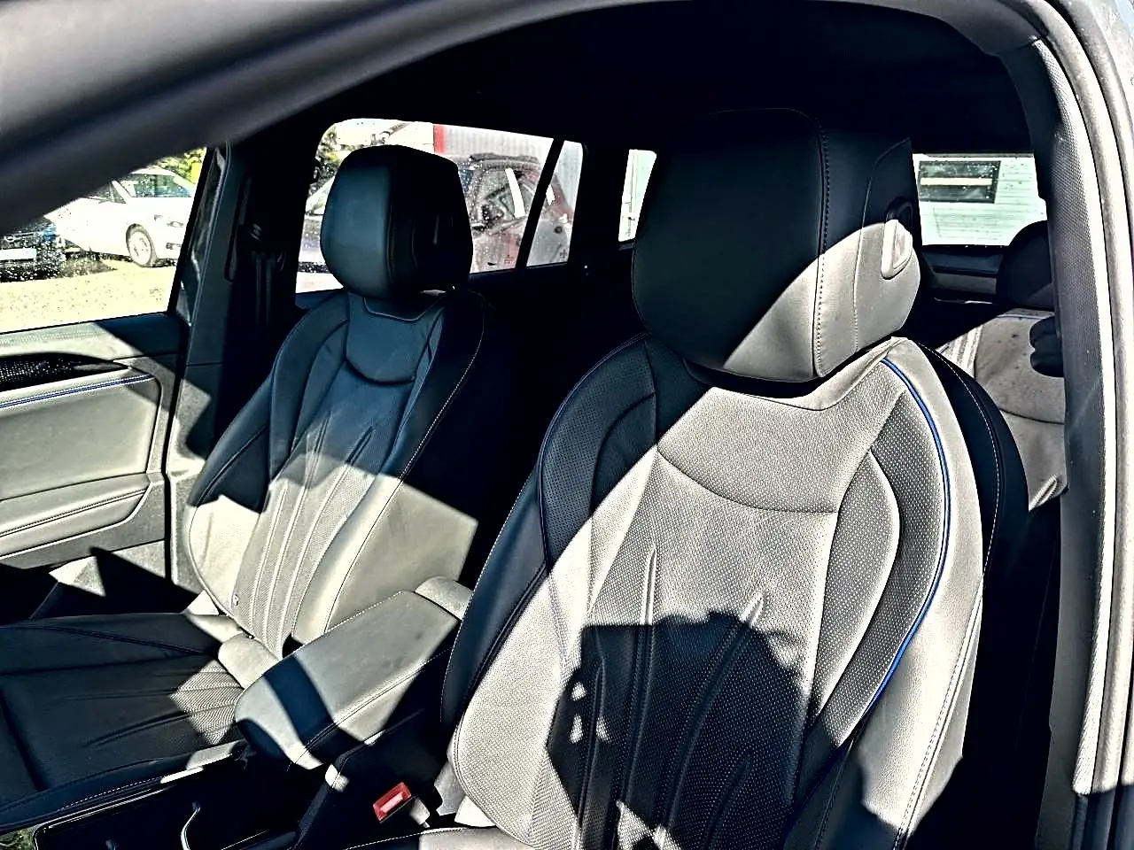 Vue intérieure côté avant droit du Volkswagen Tiguan 2024 gris dauphin, sièges cuir noir avec surpiqûres bleues et accoudoir central.